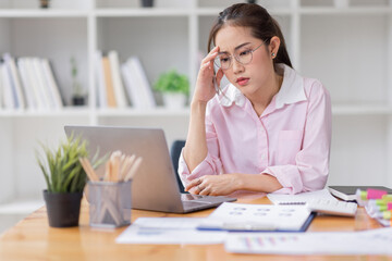 Portrait of tired young business Asian woman wear glasses work with documents tax laptop computer in office. Sad, unhappy, Worried, Depression, or employee life stress concept