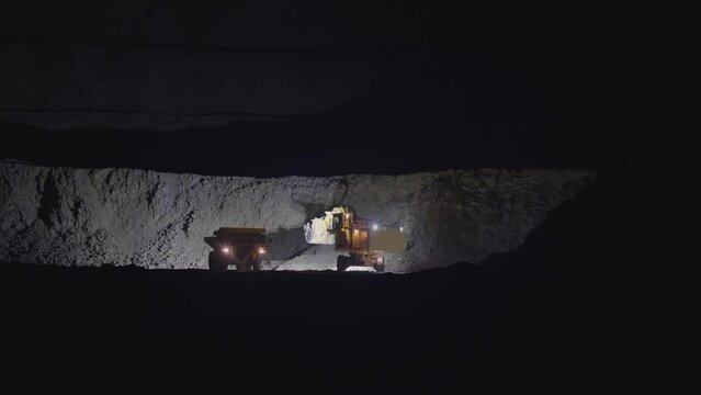 Earth mover loading dumper truck with rocks in open pit quarry mine at night, slow motion