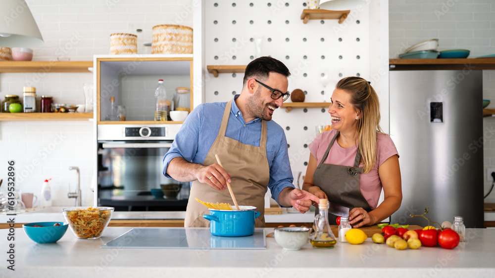 Wall mural Young happy couple is enjoying and preparing healthy meal in their kitchen together