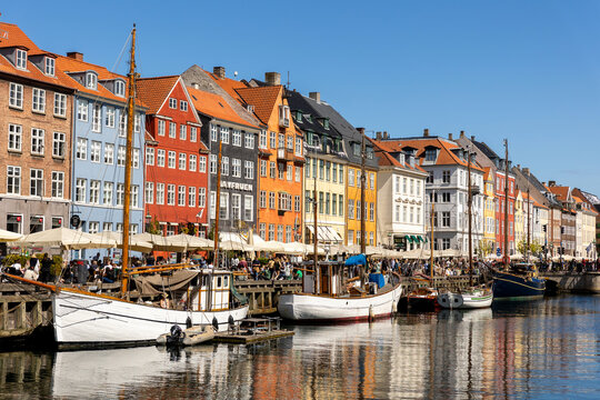 Copenhagen, Denmark - May 20, 2023: Scenic view famous colorful house building at Copenhagen Nyhavn harbour canal against blue sky on sunny day. Boats moored at european danish landmark sightseeing