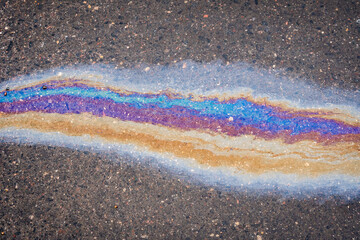 Rainbow puddle of spilled oil product on the road. Environmental pollution concept