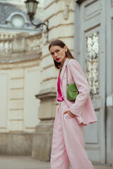 Fashionable elegant confident woman wearing trendy pink suit blazer, wide trousers, with green faux leather shoulder bag, walking in street. Outdoor fashion portrait - 619534825