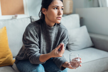 Depressed sad woman taking pills while sitting on couch at home.