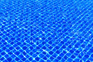 The blue tiles floor under the clear water in the swimming pool background, Swimming pool surface with floor mosaic tiles in blue