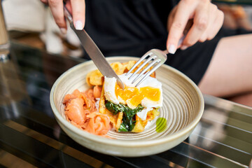 Woman cuts poached egg and yolk flows out. Potato waffles, avocado cream with salmon and egg . Healthy breakfast, protein. Restaurant dish. 