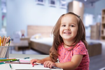 Cute small girl draws at a desk at home