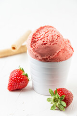 View of strawberry ice cream in white bowl on white table with two strawberries and waffles, selective focus, vertical