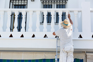 Pintor subido en una escalera pintando la fachada de una casa.	