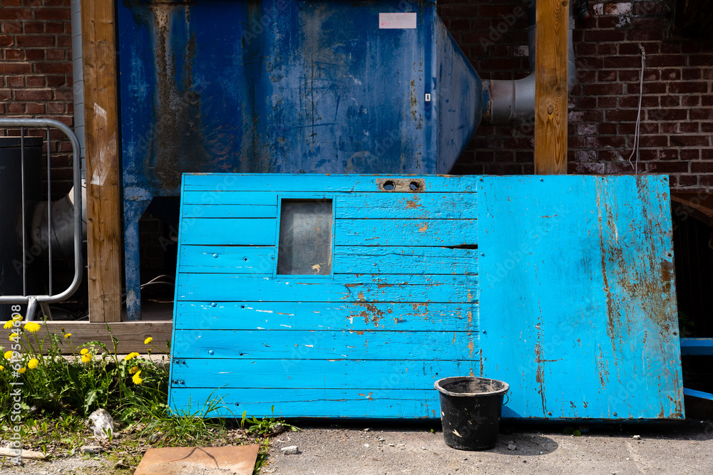 Wall mural Bright blue old wooden door leaning against the facade of an old factory building with a black bucket by the door