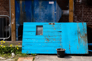 Bright blue old wooden door leaning against the facade of an old factory building with a black bucket by the door