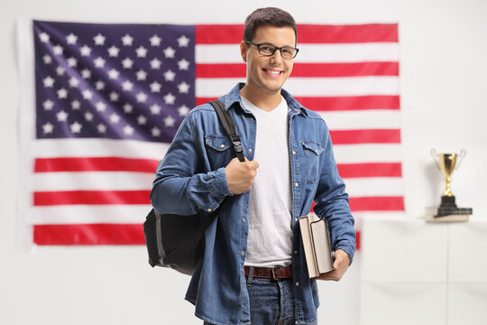 Student with a backpack and books looking at the camera and smiling in front of american flag