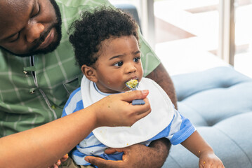 African family, father feeding baby food to her half-Nigerian half-Thai son, is 10 months old,...