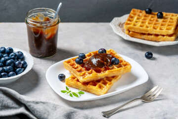 Belgian waffles with chestnut cream on white plate, blueberries, napkin and greek basil on concrete background