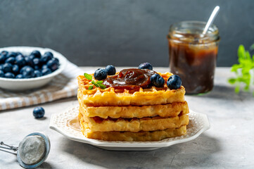 Belgian waffles with chestnut cream, blueberries, strainer with sugar powder and greek basil on concrete background