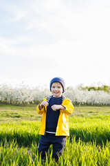 A smiling little boy in a yellow jacket runs through a blooming garden. Happy childhood.