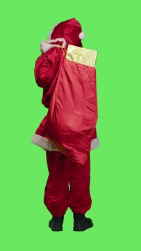 Vertical video Back view of flirty santa claus gives air kisses to spread positivity and chrsitmas spirit, acting romantic and sweet over full body greenscreen. Young man dressed as saint nick in
