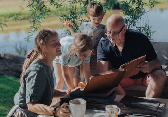 Grandpa with his grandchildren looking at old photo albums on outdoor terrace on a sunny summer day