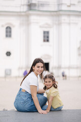 Fototapeta na wymiar Portrait of pretty young woman with her adorable daughter sitting outdoor on stone bench