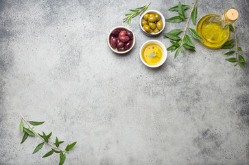 Fototapeta na wymiar Composition with green and brown olives, extra virgin olive oil in glass bottle, olive tree branches on gray concrete stone rustic background overhead, copy space border