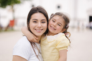 Close-up portrait of adorable daughter with beautiful mom. Little girl hug her mom