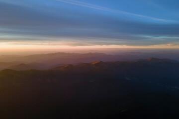 Aerial view of dark mountain hills with bright sunrays of setting sun at sunset. Hazy peaks and misty valleys in evening