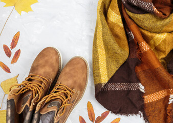 Orange leather woman bag, brown shoes, scarf, autumn leaves on gray background. Trendy autumn accessories. Cozy outfit