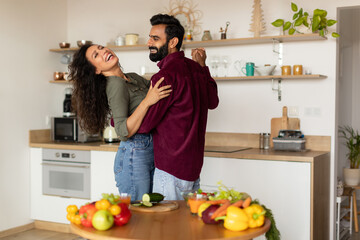 Excited arab spouses dancing together at kitchen and laughing, happy man having romantic evening with his wife at home