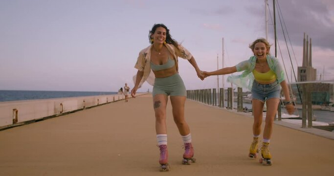 Fun And Cute Two Women In Colourful Outfits Ride Rollerblades In Slow Motion. Forever Young And Free Spirits Concept. Summer Sports Outdoor Activity