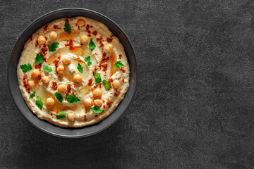 Hummus with oil and ground red pepper, chickpeas, green parsley on dark background, top view, space to copy text