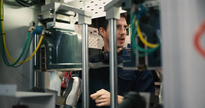 A man in a blue uniform stands behind a machine in a factory and takes advice from an employee on how to properly operate the machine. Internship at a textile factory