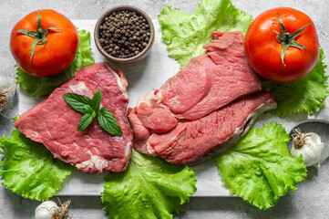 Raw beef steak meat on cutting board on rustic background with mint leaves, peppers and lettuce, butcher concept