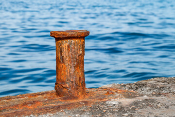 Marine bollard old metal rusty close-up on concrete embankment against background of sea, selective focus