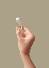 Cosmetic plastic bottle comtainer serum or essence in woman hand beige background