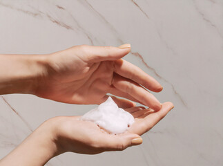 Cosmetic foam in women hands on marble background