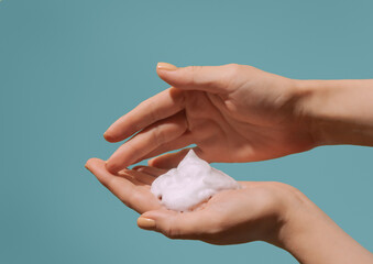 Cosmetic foam in women hands on sky blue background
