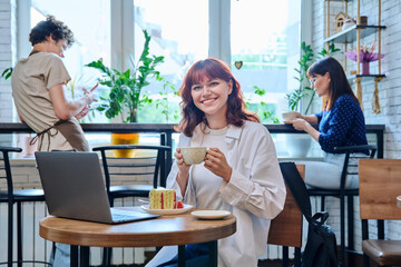 Female college student with laptop in cafe, with cup of coffee, piece of cake