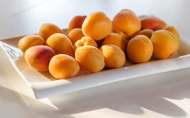 Plate with fresh apricots on white table, photo with deep shadows.