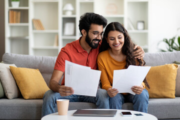 Happy young indian couple checking documents at home,