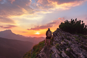 A man standing on the edge of a cliff enjoying and looking at a beautiful summer sunset in the Tatras mountains