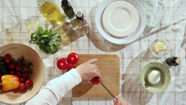 Top view image of mans hands cutting, slicing tomatoes on cutting board. Cooking at home in the kitchen. Concept of hobby, culinary, food preparation, taste, diet, healthy dish, ad