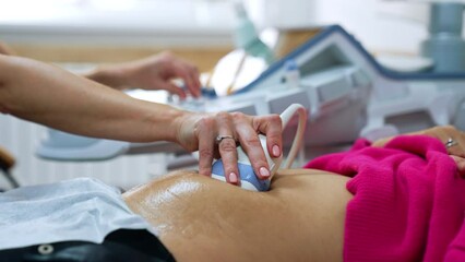 Bare female hand holds the ultrasonic device on woman's belly. Pregnancy scanning at hospital. Close up.
