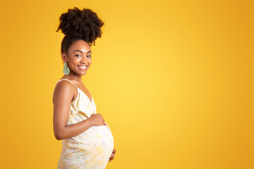 Happy young african american pregnant woman in dress touching big belly with hand