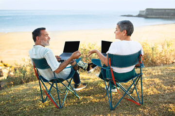 Obraz premium European Senior Spouses Using Laptop Sitting At Sea Beach Outdoor
