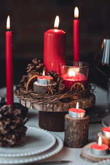 Rustic table decor for Christmas or New Year family dinner. Centrepiece with red candle, dry orange, cone, cinnamon, anise. Zero waste eco-friendly home. Cozy atmosphere, dark background. Close up