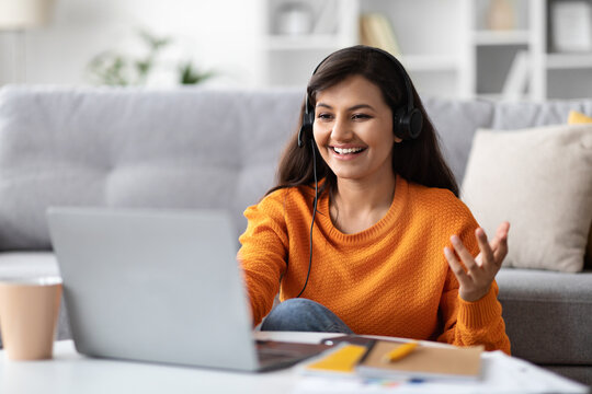 Cheerful beautiful eastern woman using headset and laptop at home