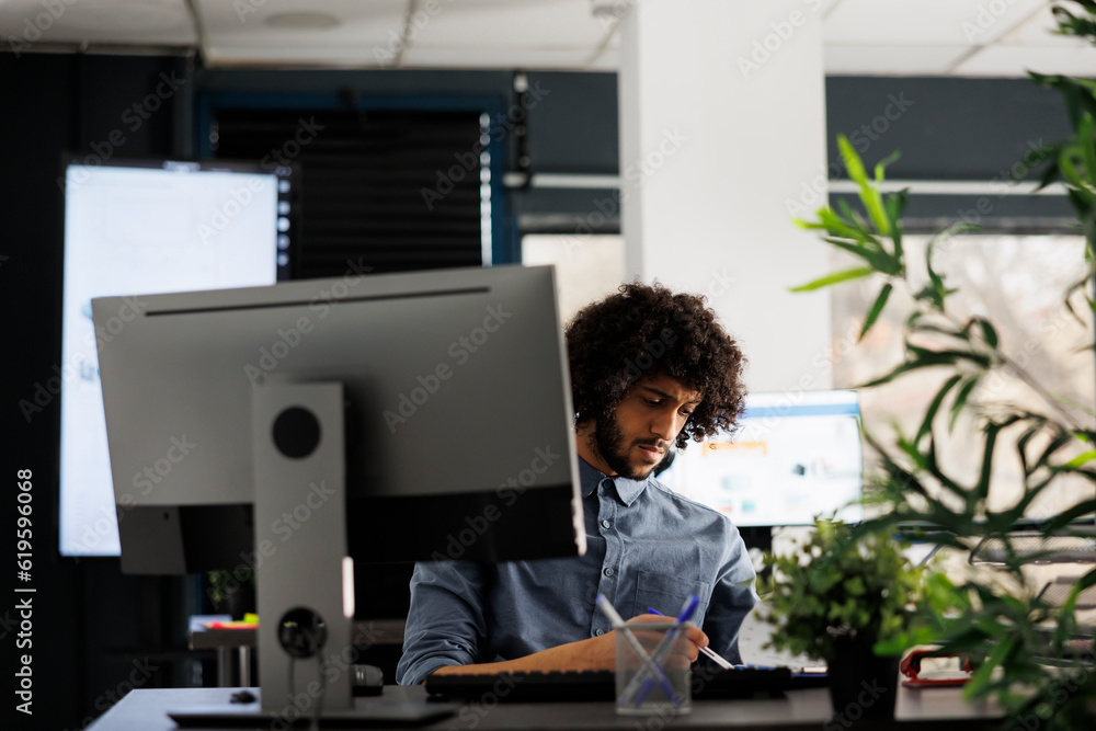 Poster arab employee analyzing marketing strategy data and working on computer at desk in business office. 