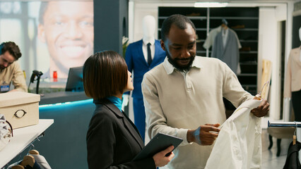 Fototapeta premium Asian store employee examining stock of trendy clothes, doing store inventory for modern fashionable collection in clothing center. Female worker using tablet, commercial activity.