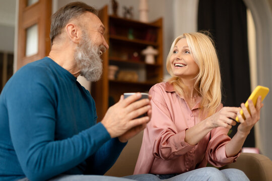 Senior Man And Woman Using Smartphone Drinking Coffee At Home