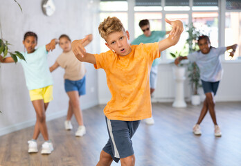 Fototapeta na wymiar Positive juvenile boy engaged in Breakdancing together with children's group in training room during workout session