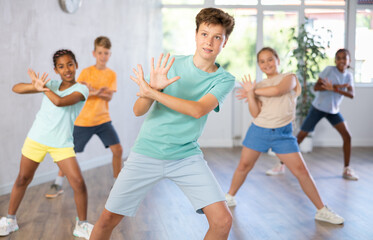 Fototapeta premium Positive boy exercising in group of classmates during dance class at dance studio